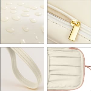 A cream PU toiletry bag with a water-resistant surface, gold zipper, sturdy handle, and organised interior compartments.