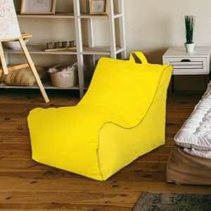 A yellow bean bag chair in a living space with wooden flooring and light furniture. It features a carrying handle.