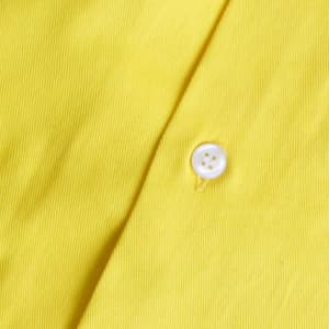 A close-up of a yellow fabric featuring a white button, part of a shirt. The texture is visible in the material.