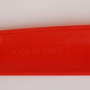 A bright red V Shaped Boomerang Toy with a smooth surface and a faint imprint indicating its place of manufacture.