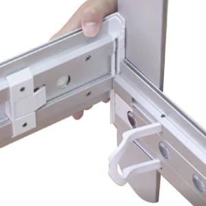 A close-up of a person's hand adjusting a white corner connector of a segmented display frame. The frame is metallic.