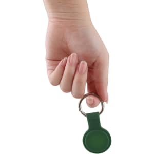 A green Air Tag protective case with a keyring, held in a hand against a white background.