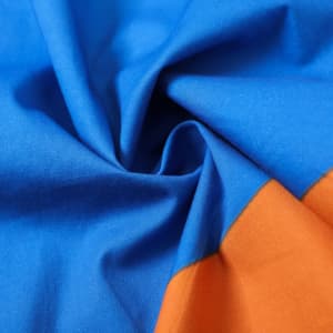 A close-up of fabric featuring vibrant blue and orange colours, showcasing smooth 100% cotton material.