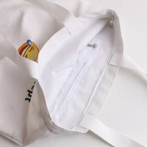 A white velvet tote bag with a zip pocket inside and dual handles. It features a logo design.