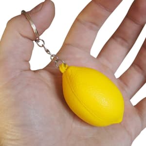 A yellow lemon-shaped stress reliever attached to a keyring, held in a hand. It has a shiny silver chain.