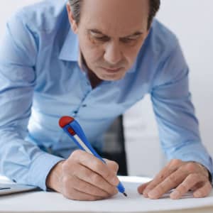 A blue and red knife-shaped ballpoint pen being used by a man in a light blue shirt while writing on paper.