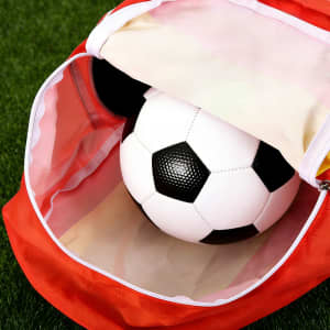 A red foldable gym bag with a white and black soccer ball inside. The bag has a logo.