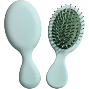 A mini paddle brush in mint green with a smooth handle and flexible bristles. The product has a simple design.