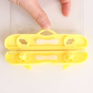 A yellow waterproof mobile pouch with a sealing mechanism, held by a hand. Features clear sides for visibility.