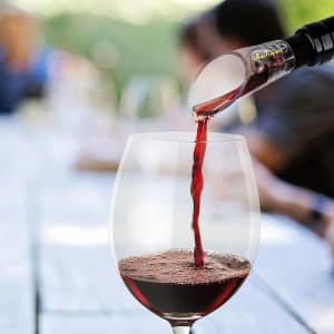 A wine aerator in use, pouring deep red wine into a clear glass, with a soft-focus background.