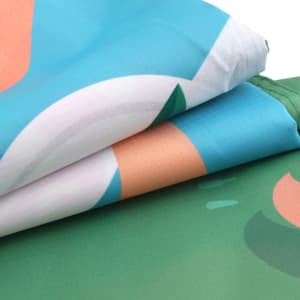 A folded outdoor blanket featuring a green, blue, and peach abstract design, with a branding logo visible.