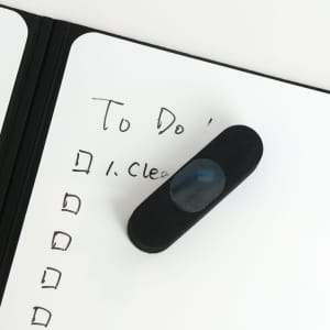 A5 whiteboard notebook with a black cover and a dark blue eraser on a handwritten to-do list.