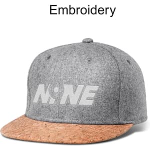 A grey snapback cap with a cork brim, featuring embroidery on the front and a logo displayed.