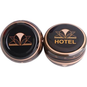 Two black tin candles with gold designs, one featuring a logo and the word "HOTEL".