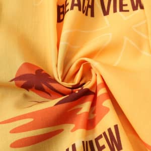 A close-up of a yellow fabric featuring beach-themed designs, including palm trees and a sunset pattern.