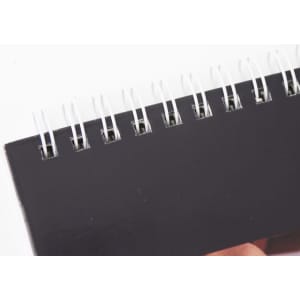 A black desk calendar with a spiral binding at the top, featuring a smooth, matte cover.