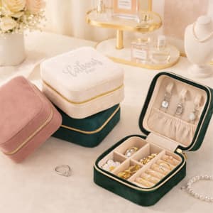 A velvet jewellery organiser in pink, green, and cream with compartments for rings and earrings. It features a logo.