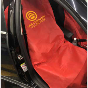 A red non-woven car seat cover with a logo, draped over the front seat of a car.