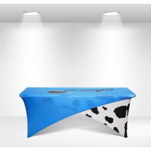 A blue and white stretch table cloth with a cow print design, fitting a 6ft table and featuring a logo.