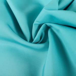 A close-up of smooth, teal fabric showcasing a soft texture with subtle draping. Features a logo in the corner.