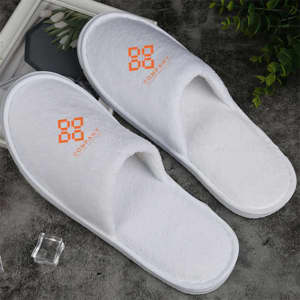White hotel slippers with a logo on the upper side, featuring a soft texture and a simple design.