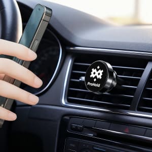 A black rotatable clip-on car phone holder is attached to an air vent, with a hand holding a smartphone nearby.