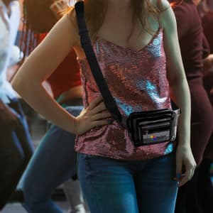 A multi-layer transparent waist bag in black worn across a sequinned top, set against a lively dance scene.