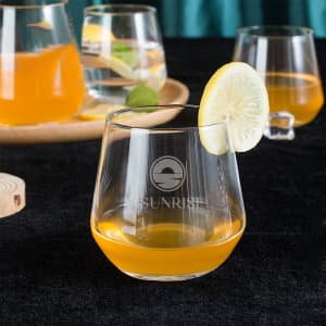 A wine glass filled with orange liquid, garnished with a slice of lemon, with additional glasses in the background.
