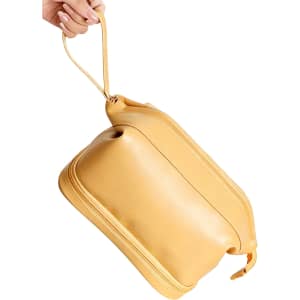 A yellow large capacity PU toiletry bag with a rounded shape and a handle, being held by a hand.