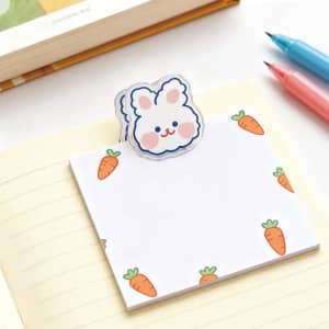 A notepad features a cute bunny-shaped clip and is decorated with small orange carrots. It has a pastel colour scheme.