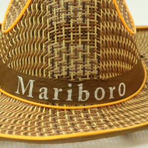 A light brown straw hat with orange accents and a fabric band featuring a logo.