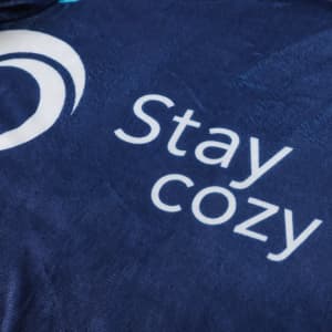 A navy blue blanket featuring a smooth texture and a logo, with the words "Stay cozy" prominently displayed.