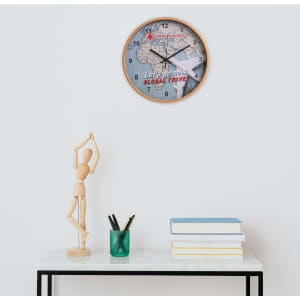 A round wall clock with a wood grain frame, featuring a map design and a logo, displayed on a stylish table.