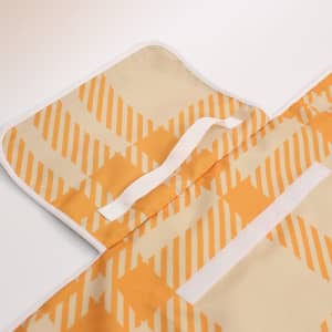 A picnic blanket with an orange and cream geometric pattern, featuring a white trim and attached straps.