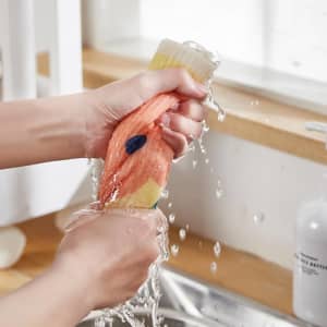 A pair of hands squeezing biodegradable dishwashing cloths under running water, featuring orange and beige colours.