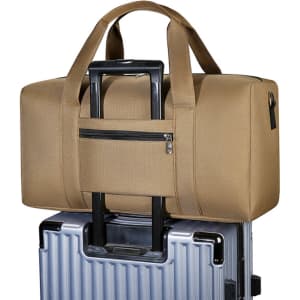 A durable duffle bag in a tan colour, featuring a zipper pocket, resting on top of a silver suitcase.