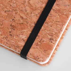 A5 cork notebook with a natural cork exterior and a black elastic band, featuring a simple white edge.
