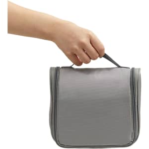 A grey hanging travel toiletry bag with a handle, being held by a hand. It features a zippered closure.