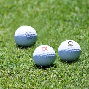 A set of three white golf balls, featuring logos, resting on green grass.