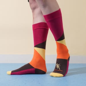 Mid-calf custom pattern socks featuring vibrant colours: pink, orange, yellow, and brown, with a logo on the foot.