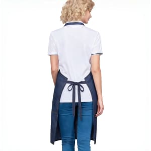 A navy denim full bib apron with a neck strap, featuring a back tie and worn over a white polo shirt.