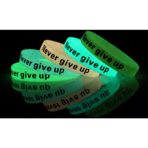 A set of glow-in-the-dark silicon wristbands in green and white with black text. They feature a motivational phrase.