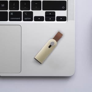 A sliding metal flash drive in gold and brown is placed on a laptop keyboard. The drive has a logo.