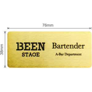 A metal name badge in gold, featuring engraved text and a logo, measuring 76mm by 38mm.
