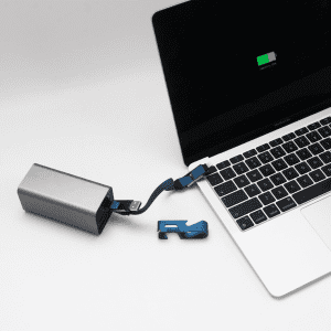 A silver power bank connected to a laptop with a blue charging cable, featuring a phone stand and opener.