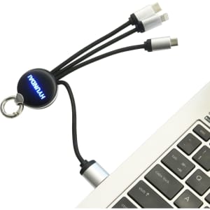A round-shaped light-up charging cable with multiple connectors, featuring a keyring attachment, displayed near a laptop.