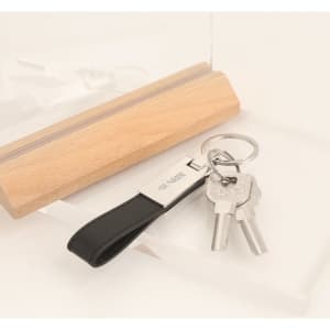 A PU leather keyring in black with a metal tag, holding two silver keys and displayed with a wooden block.