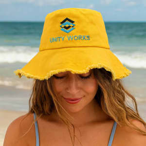 A yellow bucket hat with a frayed edge and a logo embroidered on the front, worn by a person at the beach.