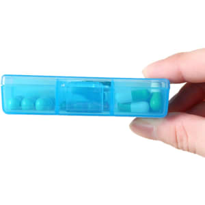 A blue square pill box with six compartments and various pills visible inside, held in a hand.