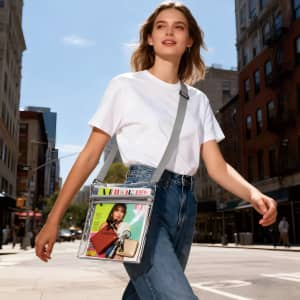 A clear PVC crossbody bag in shades of transparent and grey, holding magazines and featuring an inner pouch.